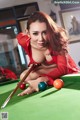 A woman in a red dress is playing pool.