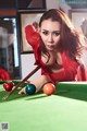 A woman in a red dress is playing pool.