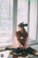 A woman sitting on a cowhide rug in front of a window.