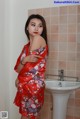 A woman in a red kimono standing in front of a sink.