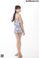 A woman standing in front of a white background wearing a gray floral romper.