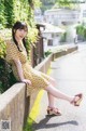 A woman in a yellow dress sitting on a wall.