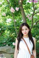 A woman in a white dress standing in front of a tree.