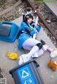 A woman sitting on the ground next to a trash can.