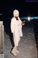 A woman in a white coat holding a sparkler in the snow.