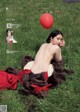 A naked woman laying in the grass with a red balloon.