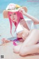 A woman with pink hair wearing a straw hat on the beach.