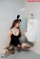 A woman in a bunny costume sitting on the floor next to a urinal.