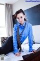 A woman in a blue shirt and tie sitting at a desk.