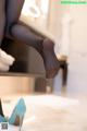 A woman in black stockings and blue high heels is putting on her shoes.