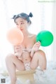 A woman sitting on a bed holding two balloons.