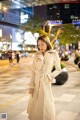 A woman in a white trench coat is walking down the street.