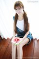 A woman sitting on a wooden floor holding a slice of watermelon.