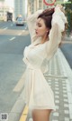 A woman in a white dress is standing on the street.