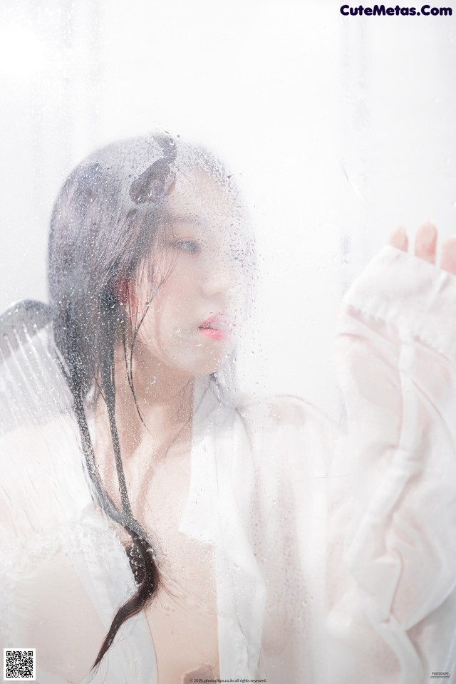 A woman in a white shirt is looking out a window.