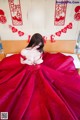 A woman in a red dress sitting on a bed.