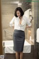 A woman in a white shirt and gray skirt standing in a bathroom.