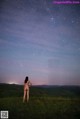 A naked woman standing in a field under a starry sky.