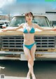 A woman in a blue bikini standing next to a yellow truck.