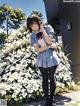 A girl in a school uniform standing in front of a bush of flowers.