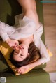 A woman laying on a green couch with her hands on her face.