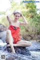 A woman in a red bathing suit sitting on a rock in the water.