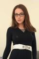 A woman wearing glasses and a black dress with a white belt.