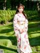 A woman in a white kimono standing in a garden.