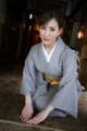 A woman in a gray kimono sitting on a wooden floor.